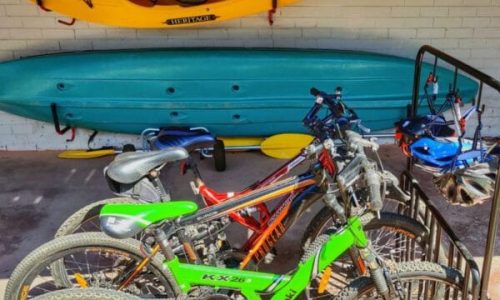 A variety of hiring equipment for exploring Gippsland Lakes, including a yellow kayak mounted on the wall, a blue canoe, and several bicycle