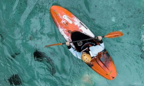 Overhead view of a person kayaking on the clear turquoise waters of Gippsland Lakes, using vibrant orange hire equipment.
