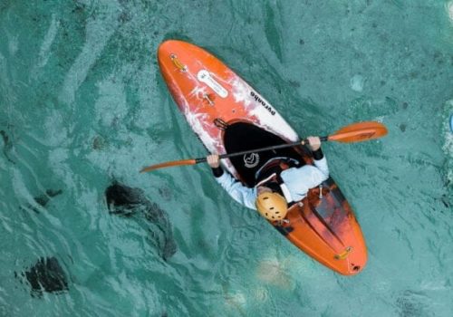 Overhead view of a person kayaking on the clear turquoise waters of Gippsland Lakes, using vibrant orange hire equipment.