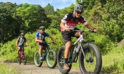 Three cyclists riding off-road bikes on a path surrounded by lush greenery, showcasing outdoor adventure opportunities at